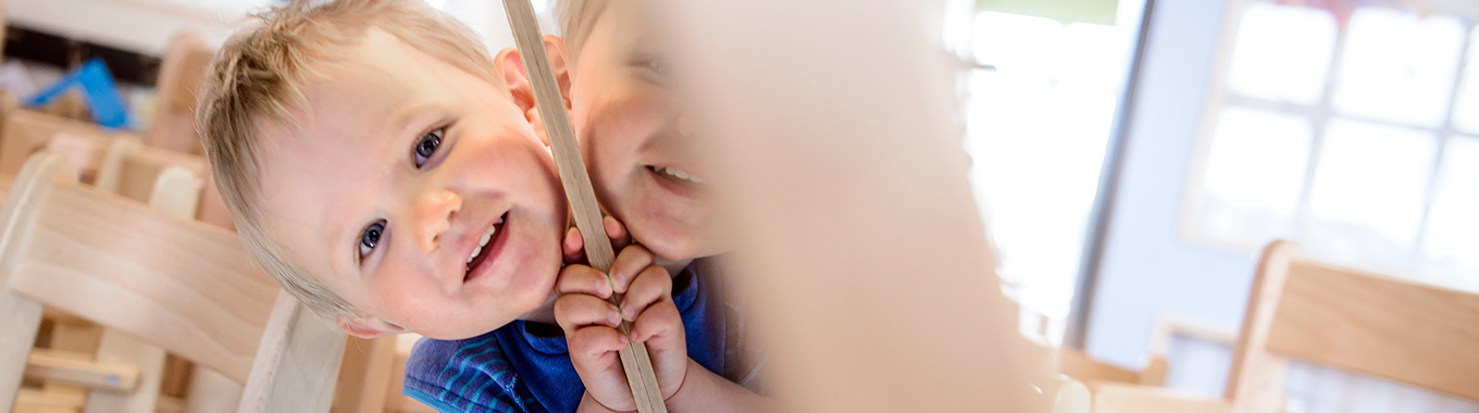 Ett litet barn tittar nyfiket fram bakom en spegel.